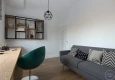 Domowe biuro w stylu lekkiego loftu z biurkiem, zielonym fotelem i szarą sofą