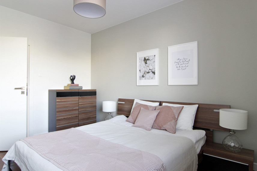 Sypialnia z drewnianym łóżkiem kontynentalnym oraz komodą stojącą z drewnianym blatem