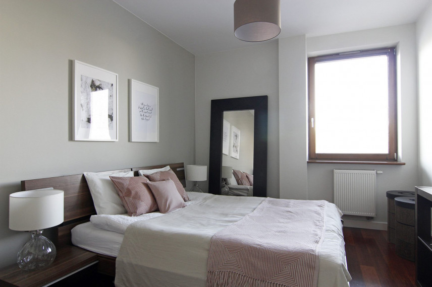 Aranżacja małej sypialni z drewnianym łóżkiem kontynentalnym oraz lustrem stojącym