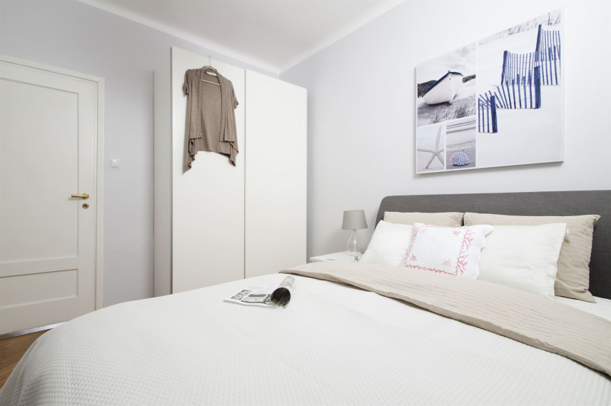 Sypialnia z szarym łóżkiem kontynentalnym oraz białą szafą z drzwiami wahadłowymi