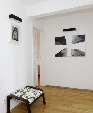 Mały, biały korytarz z siedziskiem oraz obrazami na ścianie