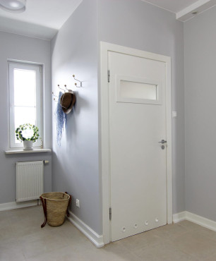 Przedpokój i korytarz z beżowymi płytkami na podłodze oraz białymi listwami podłogowymi