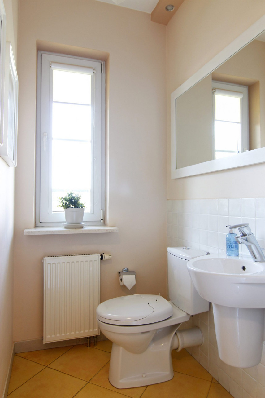 Toaleta z białym zlewem wiszącym oraz dużym lustrem w białej ramie