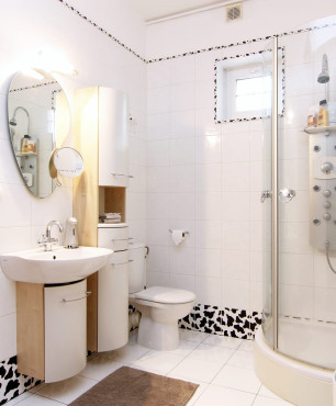 Łazienka z białymi płytkami na ścianie i podłodze oraz z ozdobnym paskiem na płytkach na ścianie