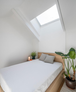 Sypialnia na poddaszu z oknem dachowym oraz drewnianym łóżkiem kontynentalnym