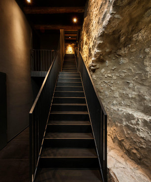 Schody jednobiegowe w korytarzu z czarną ścianą oraz z drewnianymi belkami na suficie