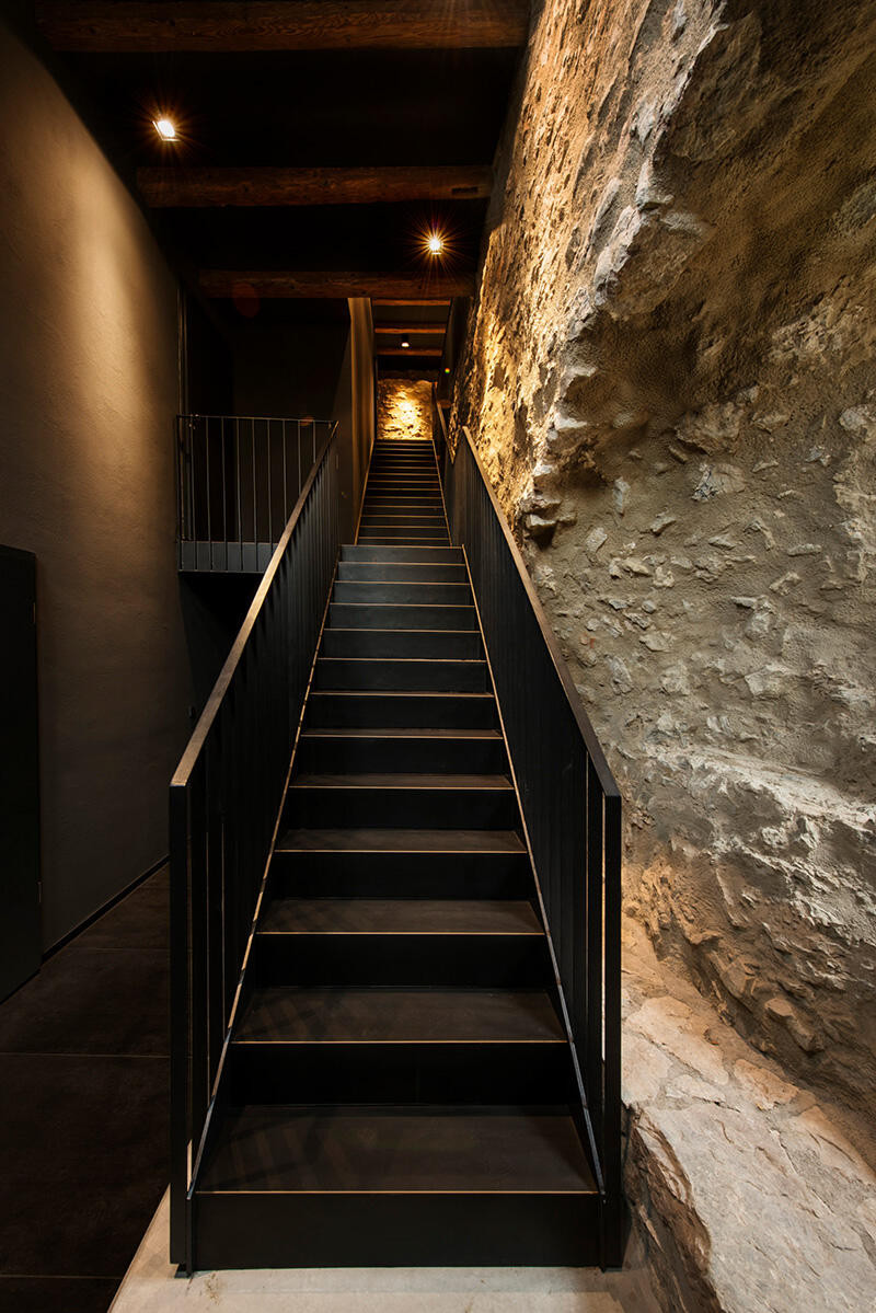 Schody jednobiegowe w korytarzu z czarną ścianą oraz z drewnianymi belkami na suficie