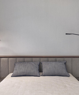 Sypialnia z łóżkiem kontynentalnym oraz z tapicerowanymi panelami na ścianie i modnym oświetleniem firmy JUNG