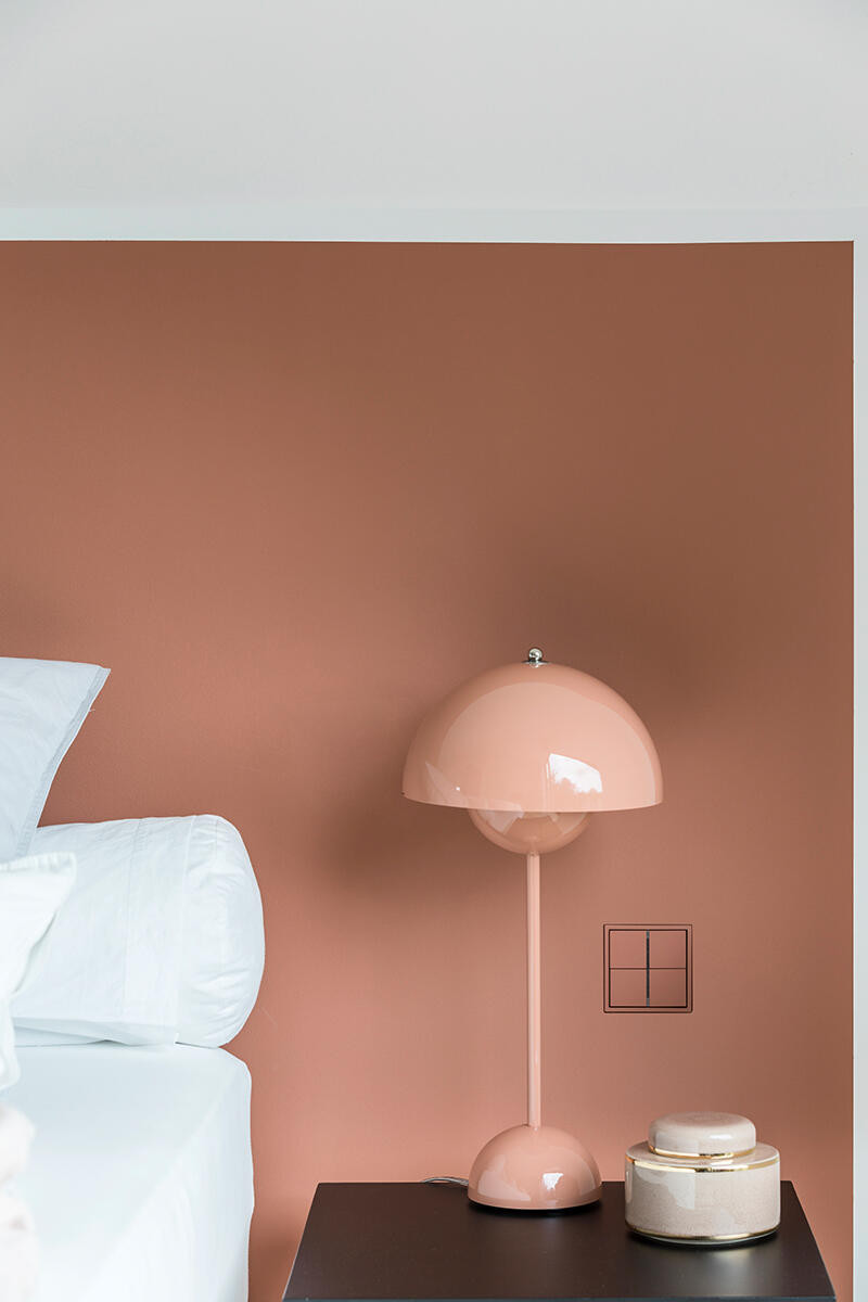 Sypialnia z brązowym kolorem ścian oraz stylową lampką stojącą