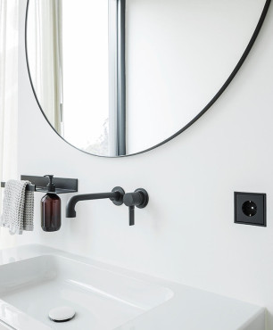 Łazienka z białym kolorem ścian oraz okrągłym lustrem w czarnej oprawie