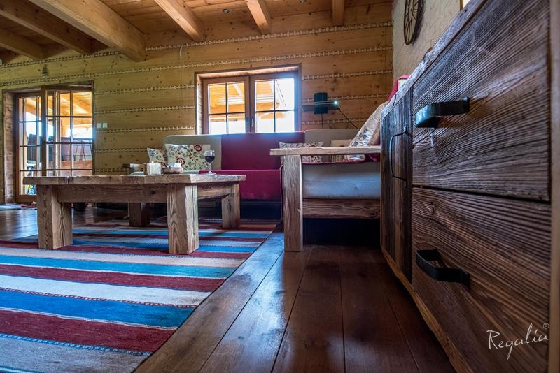 Rustykalny salon z drewnianą podłogą, boazerią na ścianie i drewnem na suficie