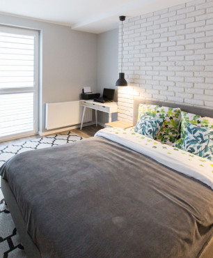 Sypialnia z dużym łóżkiem kontynentalnym oraz białą cegłą na ścianie