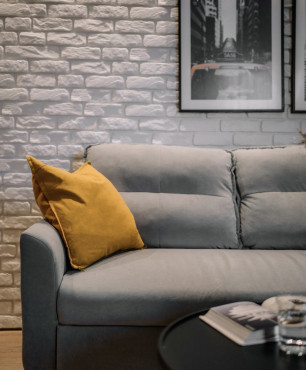 Salon z białą cegłą na ścianie oraz szarą sofą i czarnym stolikiem kawowym