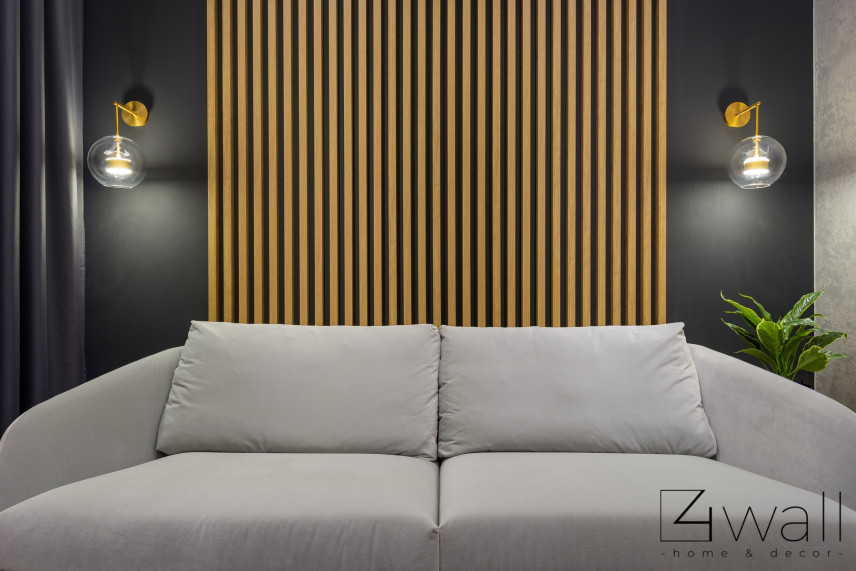Salon z szarą sofą, czarnym kolorem ścian oraz lamelem drewnianym na ścianie