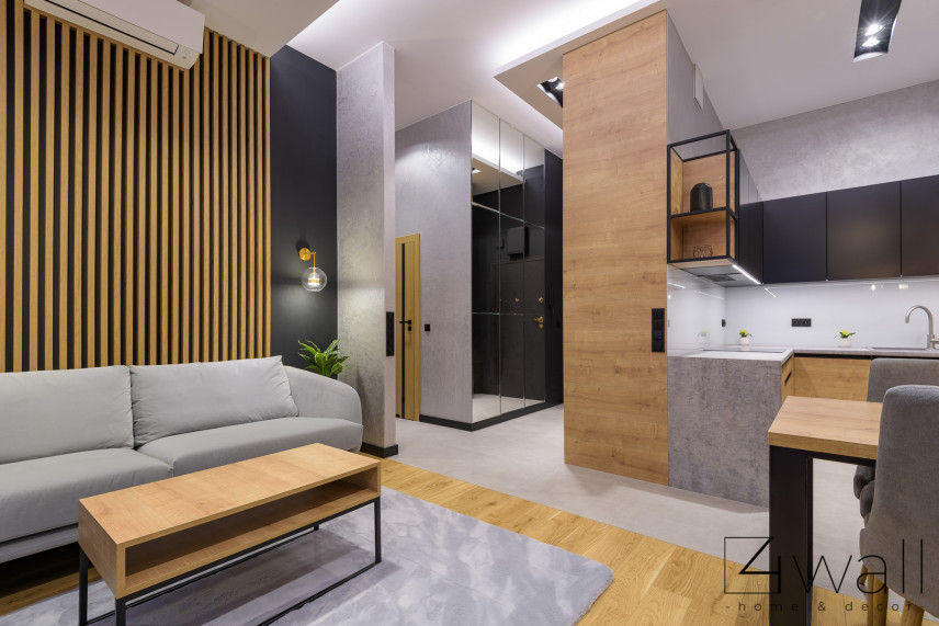 Salon, kuchnia i korytarz w przytulnym mieszkaniu z lamelem drewnianym na ścianie