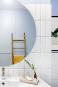 Łazienka z okrągłym lustrem oraz białymi płytkami na ścianie