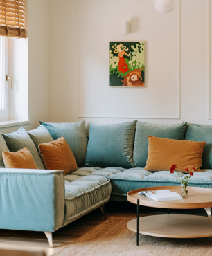 Salon z błękitnym, tapicerowanym narożnikiem oraz okrągłym, drewnianym stolikiem kawowym