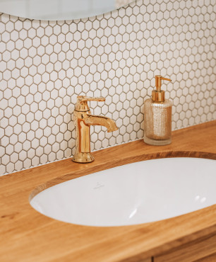 Łazienka z drewnianym blatem oraz owalną umywalką podblatową z płytkami na ścianie