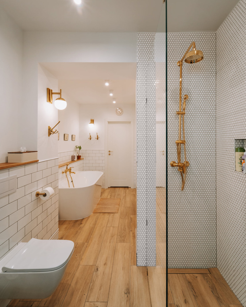 Długa łazienka z wanną owalną, ceramiczną oraz prysznicem walk-in ze złotą armaturą