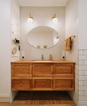 Łazienka z drewnianą szafką wiszącą oraz owalną umywalką, podblatową i złotymi dodatkami