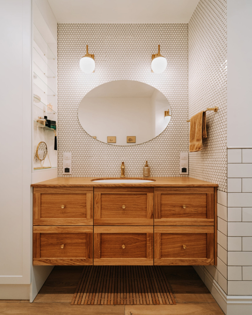 Łazienka z drewnianą szafką wiszącą oraz owalną umywalką, podblatową i złotymi dodatkami