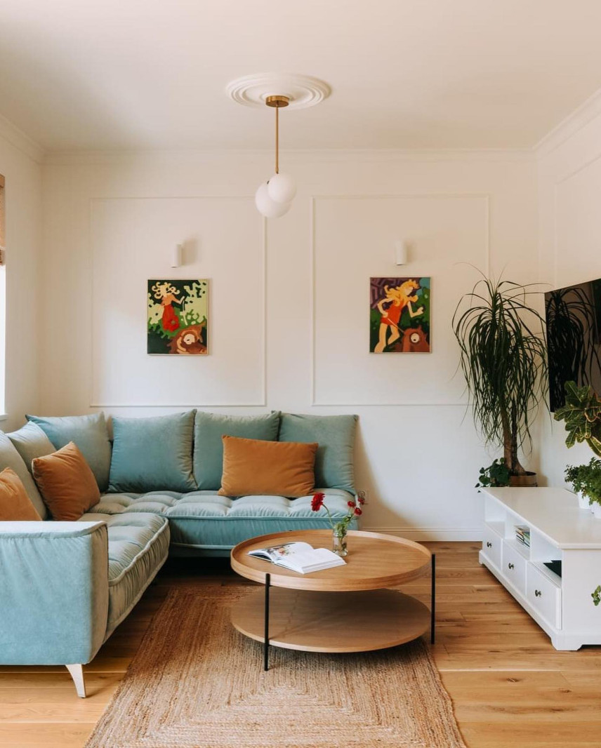 Salon z narożnikiem w kolorze błękitnym, sztukaterią i telewizorem na ścianie  oraz bambusowym dywanem