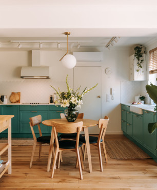 Kuchnia otwarta z zielonymi frontami meblowymi oraz z okrągłym stolikiem z drewnianymi krzesłami