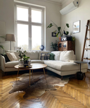 Salon w mieszkaniu w wysokiej kamiennicy z drewnianym parkietem oraz dywanem ze skóry dzika