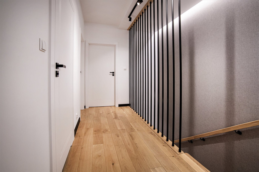 Długi korytarz z jasnymi panelami na podłodze i białym kolorem na ścianie