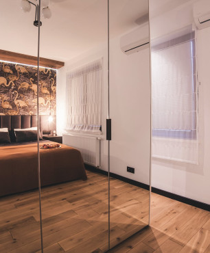 Sypialnia z tapicerowanym łóżkiem oraz szafą w zabudowie z lustrzanym frontem i ciemną podłogą