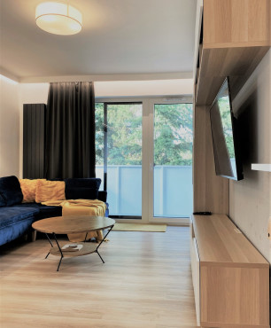 Salon w mieszkaniu w bloku z telewizorem na ścianie oraz z meblościanką z drewnianymi frontami