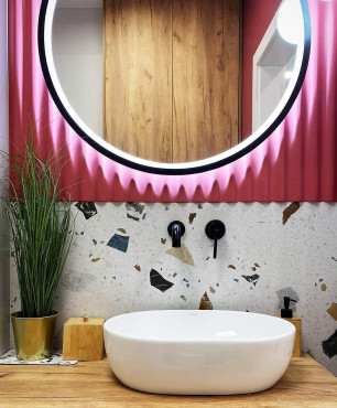 Łazienka z różowym akcentem na ścianie, okrągłym lustrem oraz lastryko