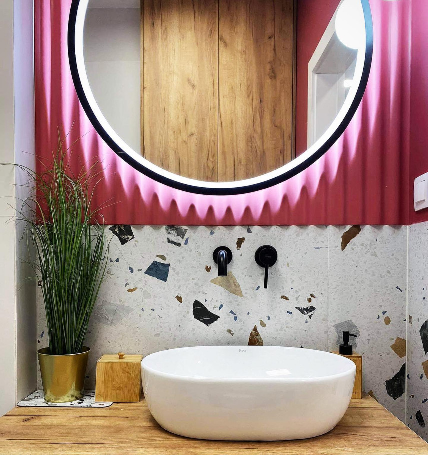 Łazienka z różowym akcentem na ścianie, okrągłym lustrem oraz lastryko