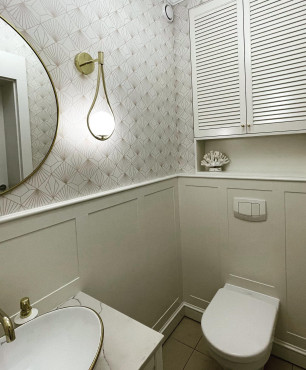 Mała toaleta z tapetą na ścianie, złotym kinkietem oraz złotym kranem