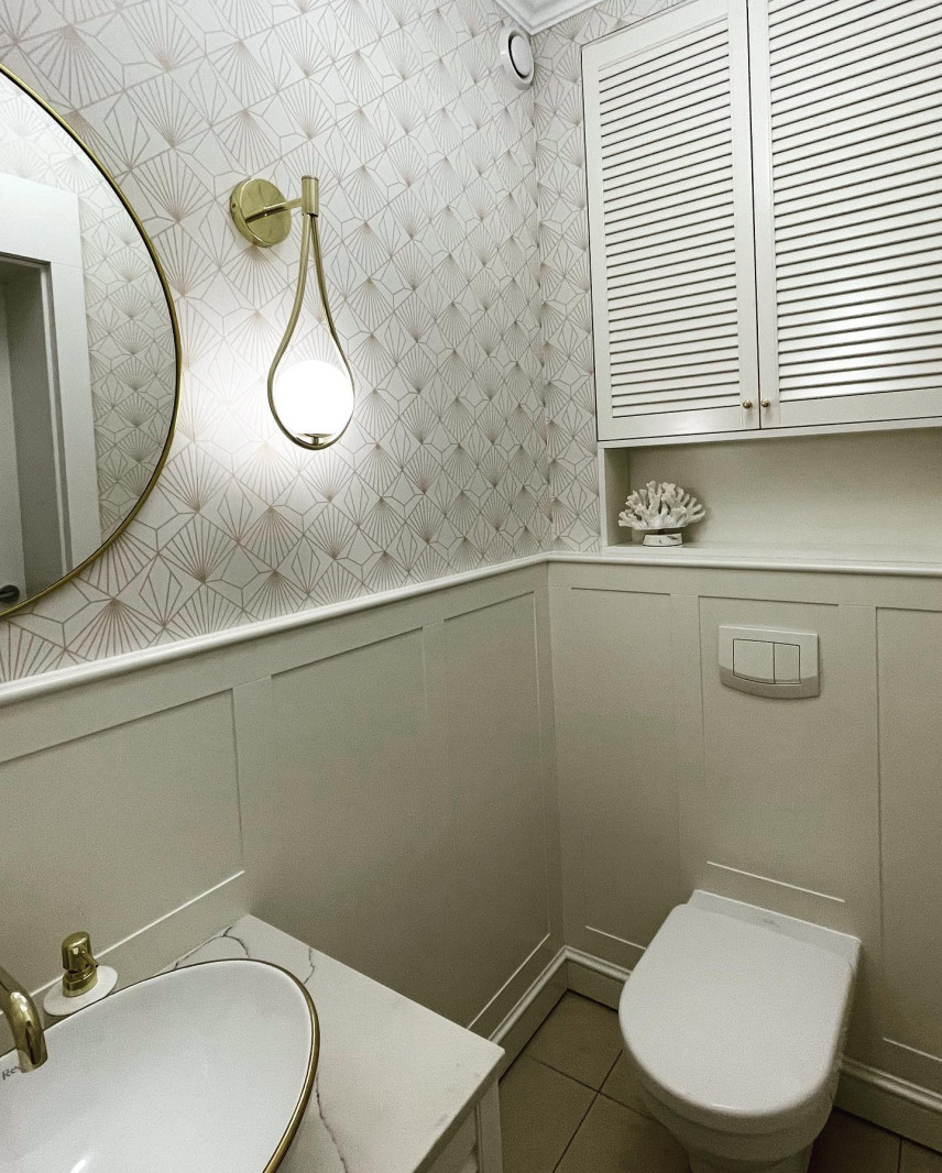 Mała toaleta z tapetą na ścianie, złotym kinkietem oraz złotym kranem
