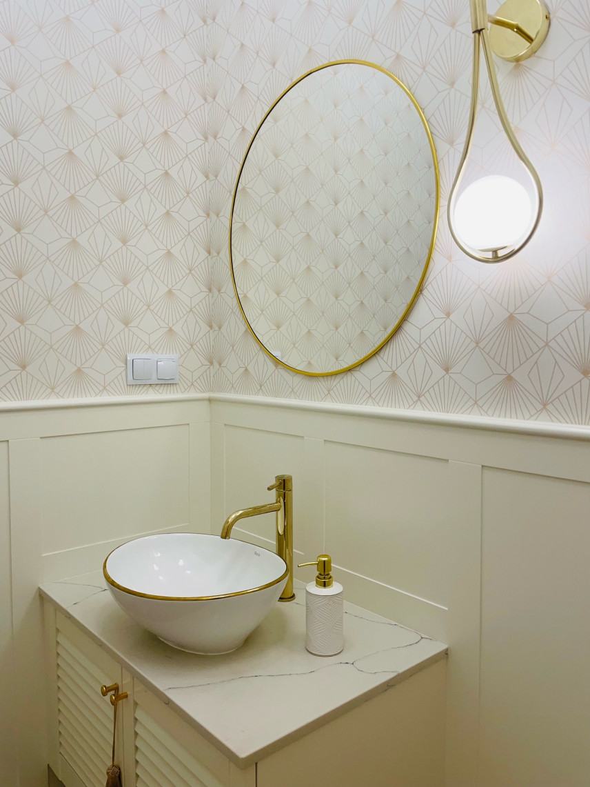 Toaleta z okrągłym lustrem w złotej ramie, białym blatem z szarym spiekiem kwarcowym oraz złotym kranem