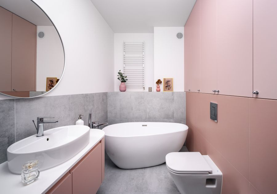 Łazienka w pastelowych kolorach z wanną wolnostojącą oraz z szarymi, wielkoformatowymi płytkami na ścianie