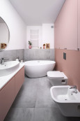 Podłużna łazienka z wanną owalną, ceramiczną, muszlą wiszącą, bidetem oraz szarymi płytkami wielkoformatowymi na ziemi