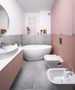 Podłużna łazienka z wanną owalną, ceramiczną, muszlą wiszącą, bidetem oraz szarymi płytkami wielkoformatowymi na ziemi