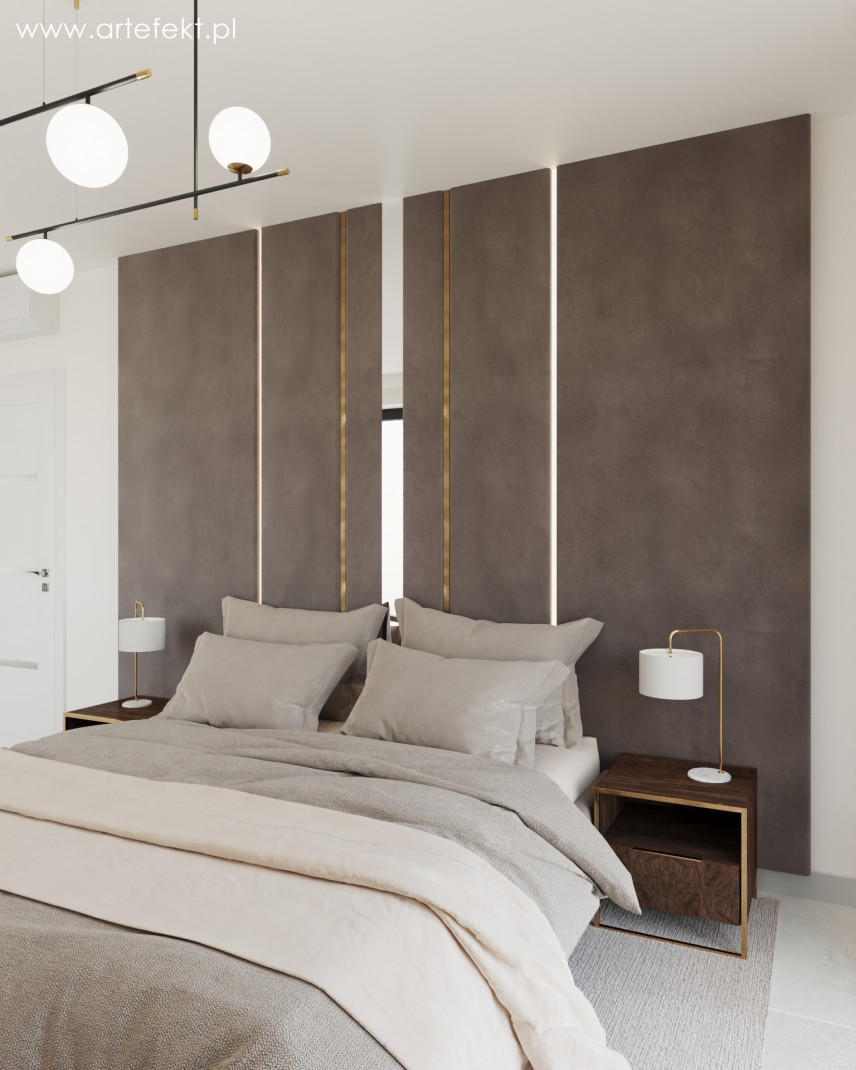 Sypialnia z tapicerowaną ścianą, dużym łóżkiem kontynentalnym, szafkami nocnymi z lampkami oraz szarym dywanem na podłodze