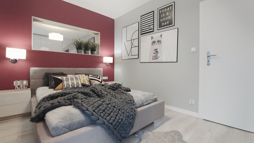 Sypialnia z czerwonym kolorem na ścianie z prostokątnym lustrem oraz z tapicerowanym łóżkiem kontynentalnym