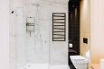 Łazienka z prysznicem i białymi płytkami na podłodze i ścianie oraz z czarnym kaloryferem