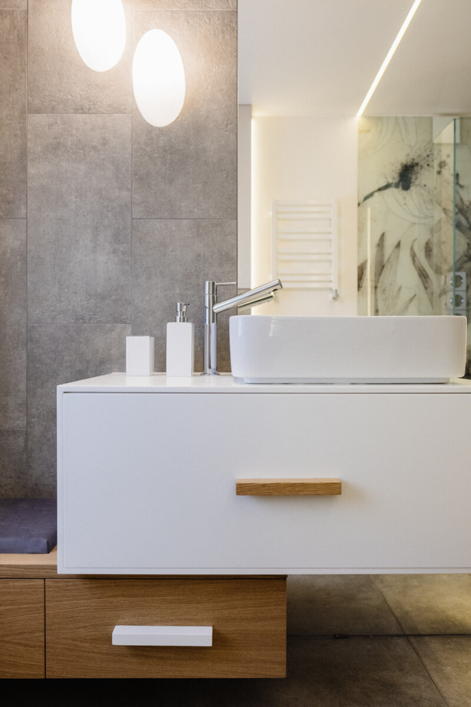 Łazienka z szarymi płytkami na ścianie oraz biało-drewnianą szafką z umywalką nablatową