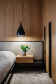 Sypialnia z drewnem na ścianie oraz lampą wiszącą z czarnym kloszem
