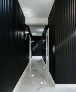 Długi korytarz z czarnym kolorem na ścianie oraz białymi, gresowymi płytkami na podłodze
