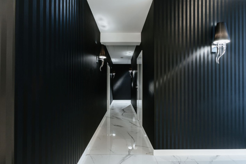 Długi korytarz z czarnym kolorem na ścianie oraz białymi, gresowymi płytkami na podłodze