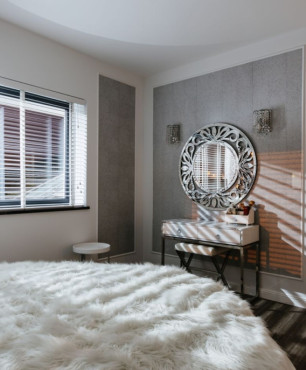 Piękna sypialnia z dużym oknem, imitacją betonu na ścianie, toaletką z okrągłym lustrem