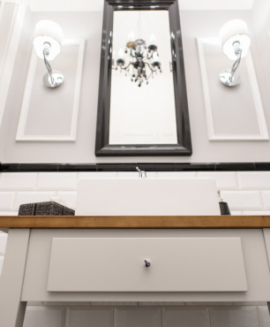 Modna toaleta z białą szafką stojącą z drewnianym blatem oraz z czarnym, kryształowym żyrandolem
