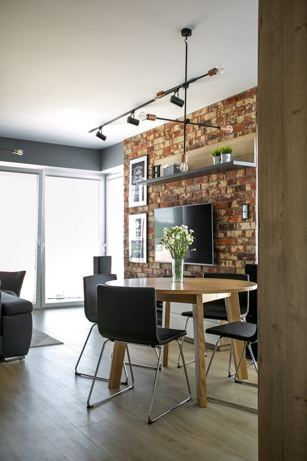 Salon w stylu industrialnym z cegłą na ścianie oraz z kącikiem jadalnianym z okrągłym stołem