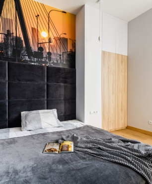 Sypialnia z dużym, kontynentalnym łóżkiem oraz z panelami tapicerowanymi w kolorze czarnym
